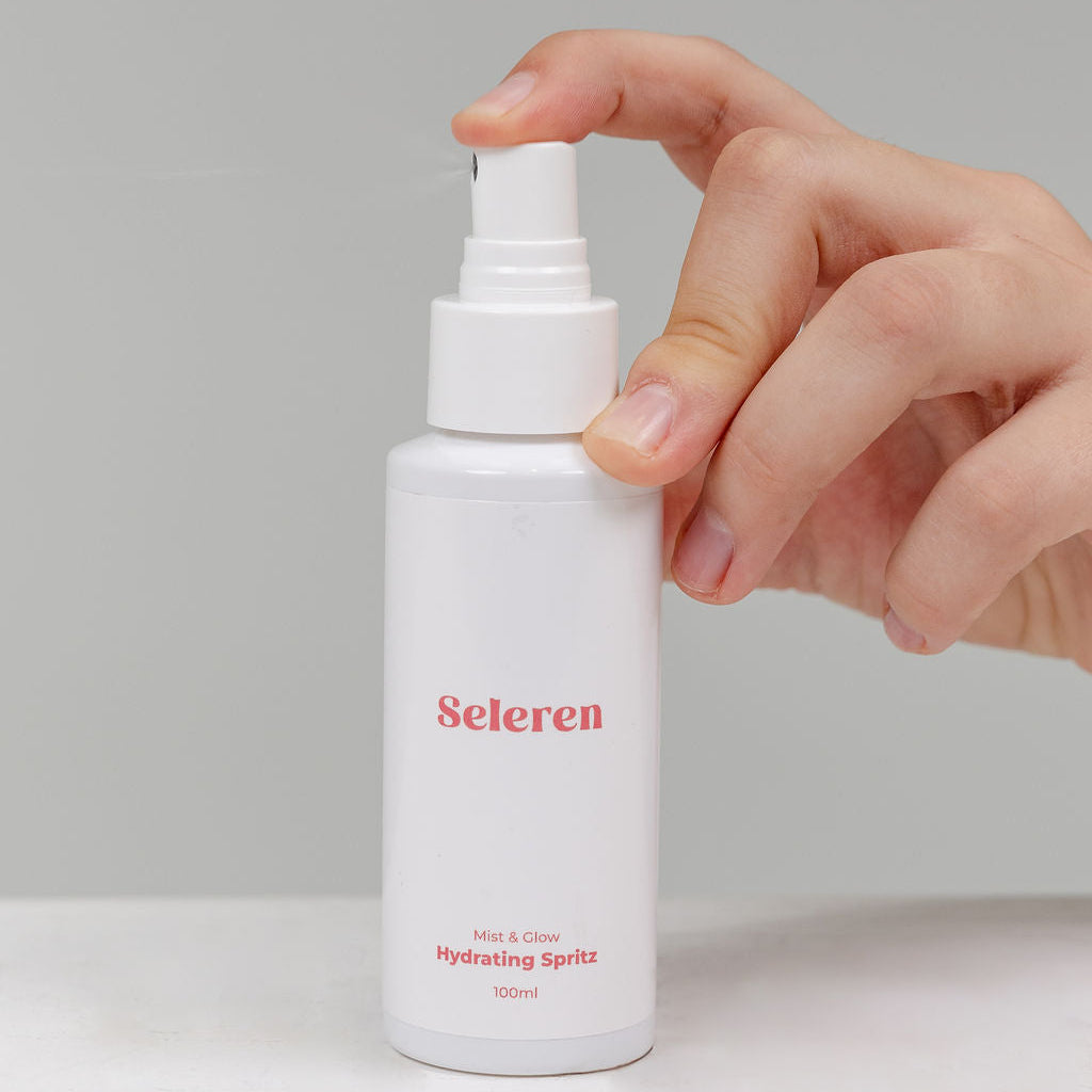 Hand holding a white Mist & Glow Hydrating Spritz spray bottle labeled 'Seleren' against a light gray background