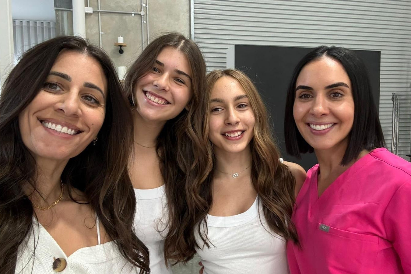Four women posing together in a room with a neutral background