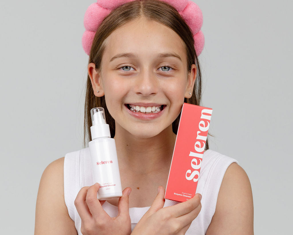 A smiling young girl with a pink headband holds a white Seleren 
bottle and a coral-pink box labeled 'Seleren' against a solid gray background.