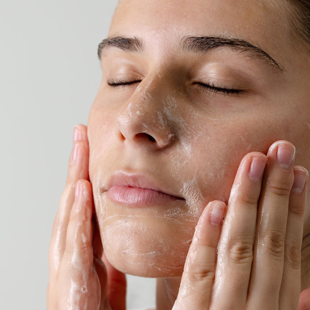 Teen woman applying Seleren cleansing her to her face with a neutral background