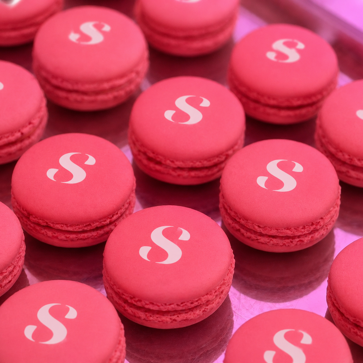 Watermelon pink macarons with a white 's' Seleren logo icon on a reflective surface