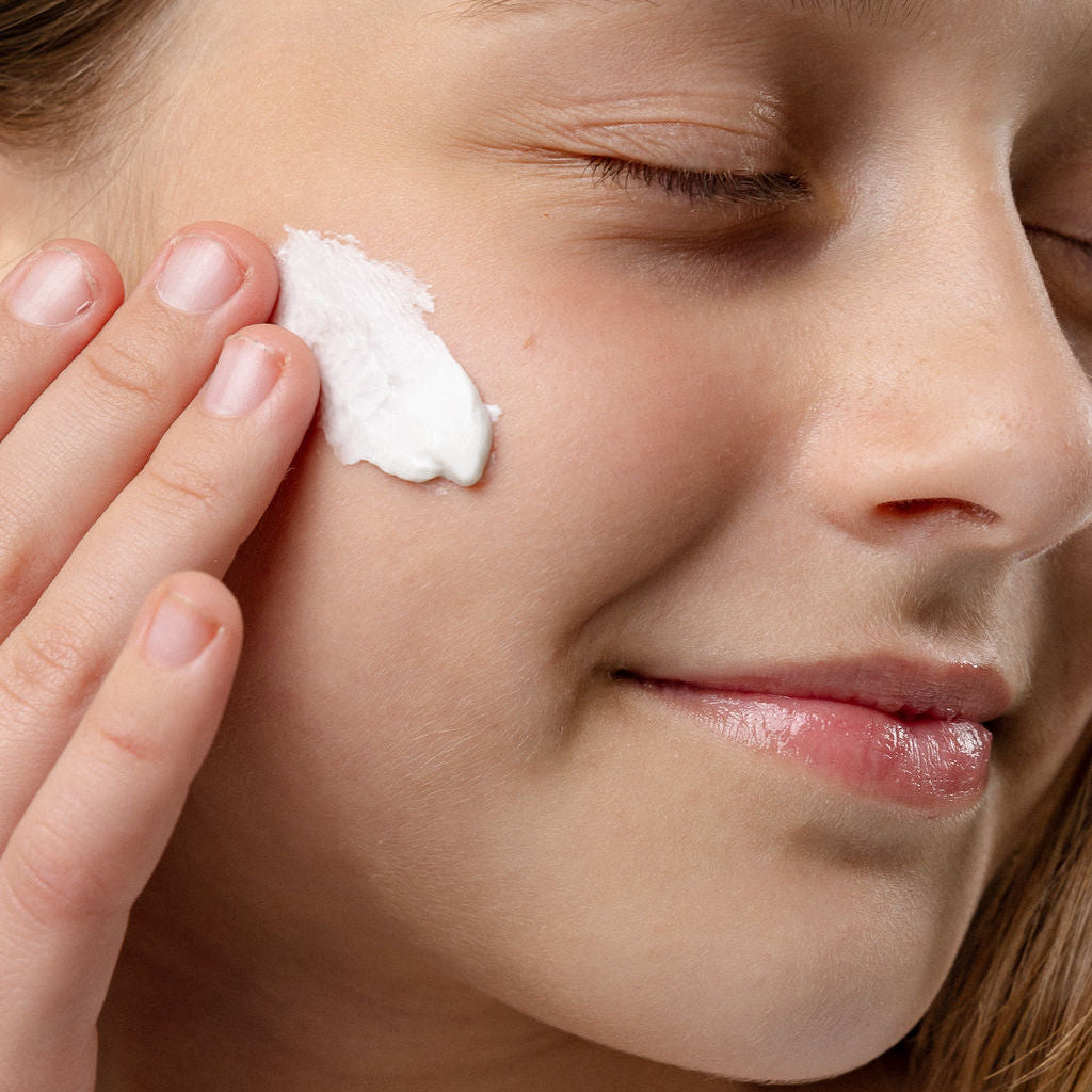 Tween woman applying Seleren Calm and Quench Nourishing Mask to her face with a close-up view